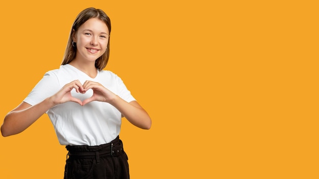Liefde teken Ondersteunende tiener Zorg vertrouwen Aanmoediging waardering Enthousiast gelukkig meisje in het wit weergegeven: hart gebaar glimlachend geïsoleerd op oranje kopie ruimte promotionele achtergrond