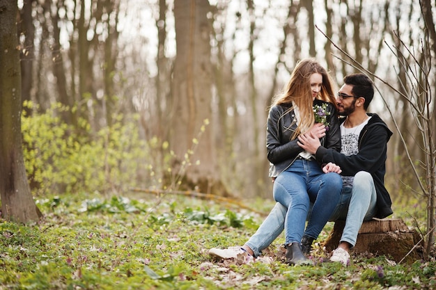 Liefdesverhaal van een cool multiraciaal stel in het voorjaarsbos Ze zitten op een boomstronk