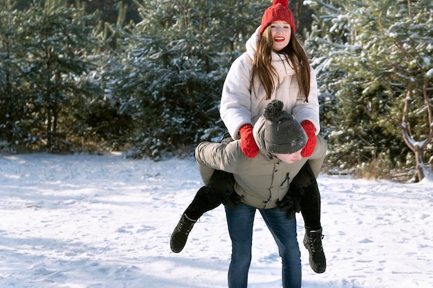 Liefdevol jong stel heeft plezier in de winter buiten Guy rolt meisje op zijn rug Besneeuwd bos