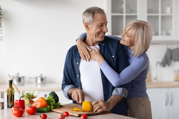 Liefdevol senior koppel dat samen gezonde salade maakt in de keuken