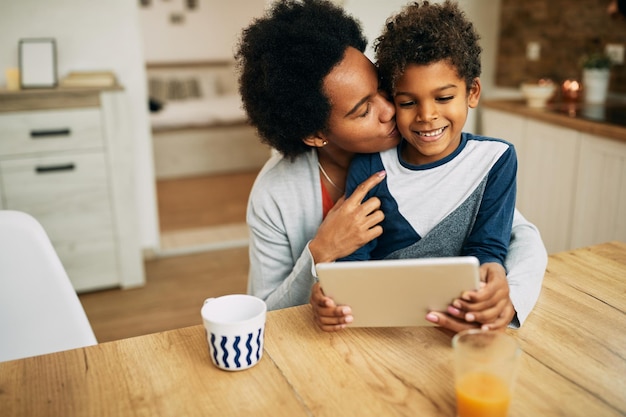 Liefdevolle Afro-Amerikaanse moeder en zoon die thuis digitale tablet gebruiken