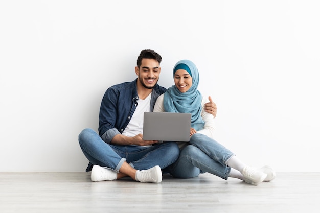 Liefdevolle familie zittend op de vloer met laptop in lege kamer