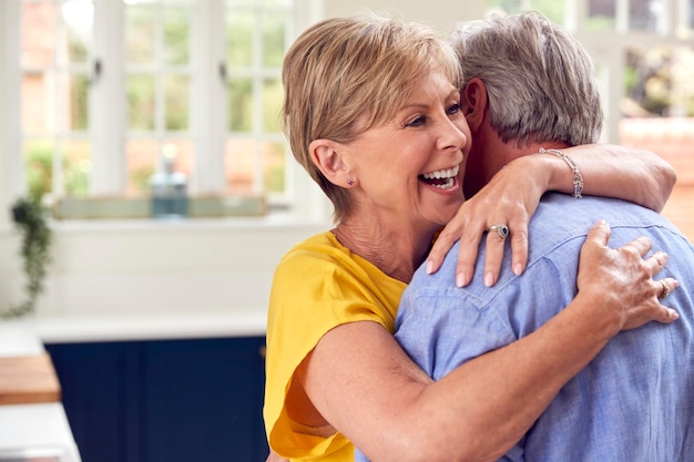 Liefdevolle gepensioneerd koppel knuffelen in de keuken thuis samen