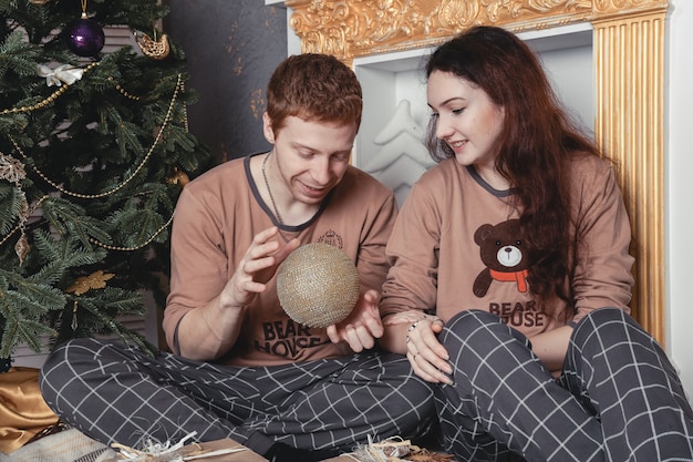 Liefdevolle jong koppel zittend op de vloer door kerstboom op kerstochtend, strelen.