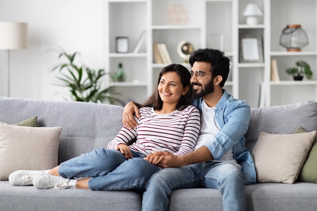 Liefdevolle oosterse millennial man en vrouw die thuis knuffelen.