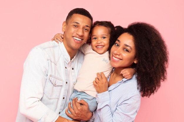 Liefdevolle zwarte ouders en kleine dochter delen een warme knuffel vader moeder en vrouwelijk kind glimlachend