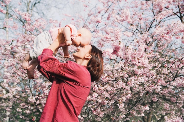 Liefhebbende moeder en babymeisje op achtergrond bloeiende roze bloemen van appelboom in de lente