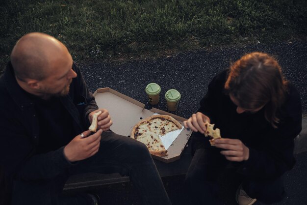 Liefhebbers eten pizza zittend op het gazon tijdens zonsondergang bovenaanzicht