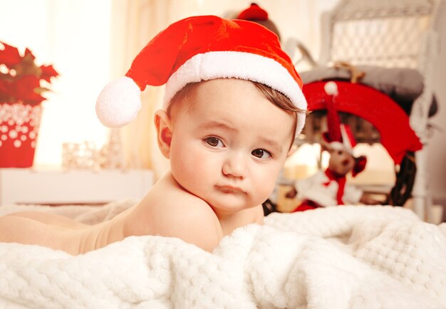 Lieve baby met kerstmuts op een knus dekentje en kerstversieringen op de achtergrond