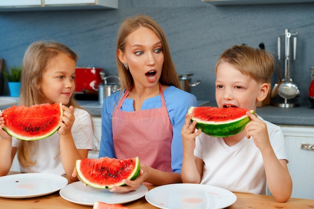 Lieve familie, moeder en haar kinderen die watermeloen eten in hun keuken met plezier