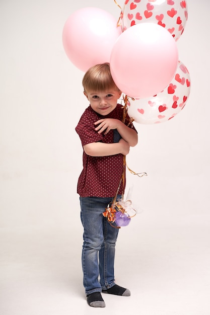 Lieve jongen die ballonnen vasthoudt met rode en roze harten Valentijnsdag of medische zorgconcept voor kinderen