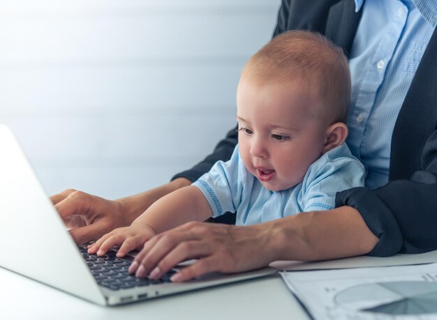 Lieve kleine baby speelt met laptop en lacht terwijl hij op de knieën van zijn moeder zit