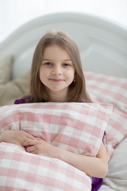 Lieve kleine donkere haren meisje met cushin zit op bed