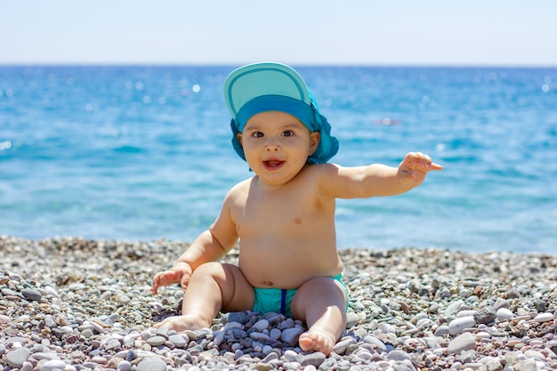 Lieve mollige baby op een kiezelstrand. Blauwe zee en zomerzon