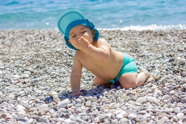 Lieve mollige baby op een kiezelstrand. Blauwe zee en zomerzon