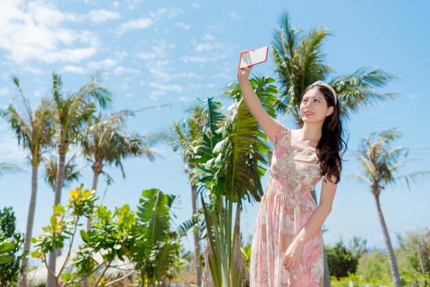 lieve vrouw die naar tropische natiereizen gaat en mobiele smartphone gebruikt die een selfie-foto maakt met kokospalm.