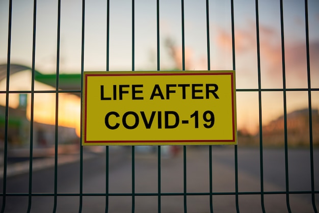 Life After COVID-19 sign on a fence with blured city view at sunset