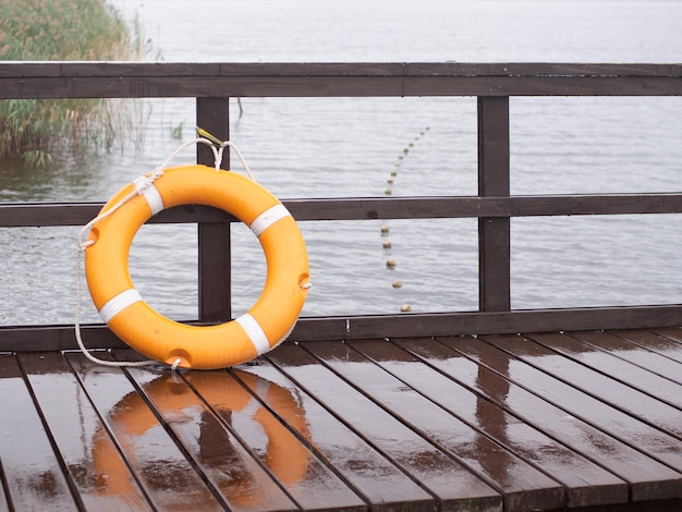 Life belt on a fenced pier on a foggy rainy morning closeup with selective focus and copy space