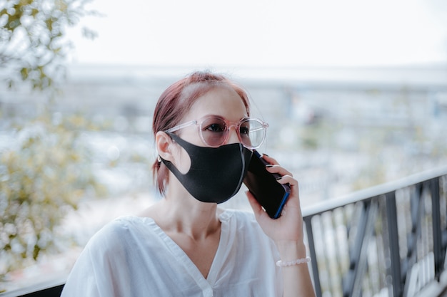 写真 covid-19パンデミック中の生活。アジアの女性は、街で医療用マスクとスマートフォンを使用します。