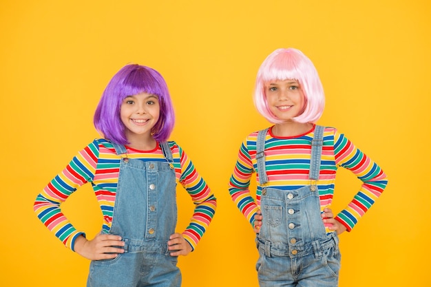 Life is better with friends happy girls friends on yellow\
background little friends smile in fashionable hair wigs and\
stylish overalls adorable small friends enjoy friendship\
playmates