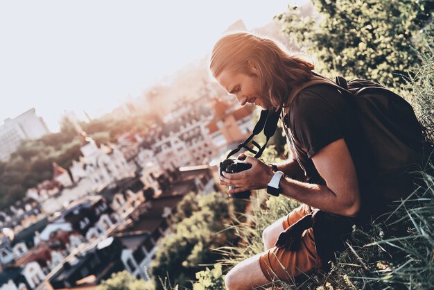 Life is full of beauty. Young man in casual clothing using camera and smiling 