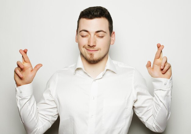 Life style business and people concept business man in shirt keeping fingers crossed while standing against white background