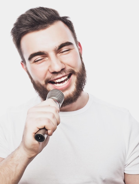 Life style concept: a young man with a beard wearing a white shirt holding a microphone and singing.Isolated on white. Special Fashionable toning photos.