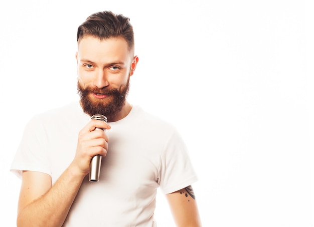 Концепция образа жизни: молодой человек с бородой в белой рубашке держит микрофон и поет. Изолированные на белом.