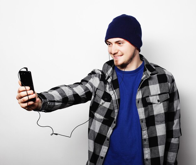 Life style, education and people concept: young  man listening to music and using smartphone, while standing against grey background.