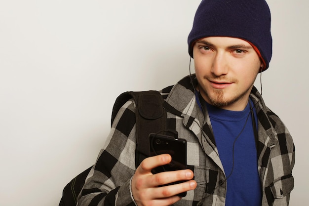 Life style education and people concept young man listening to music and using smartphone while standing against grey background