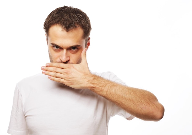 Life style  and people concept: Shocked young man  covering mouth with hands and looking at camera while standing against white background