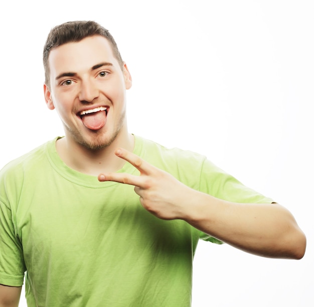 Life style and people concept: young casual man showing the victory gesture while smiling for the camera with a hand in his pocket.Isolated on white background