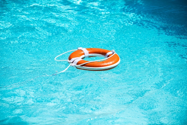 Lifebelt on sea or pool orange inflatable ring floating in blue water life buoy for protect and safe