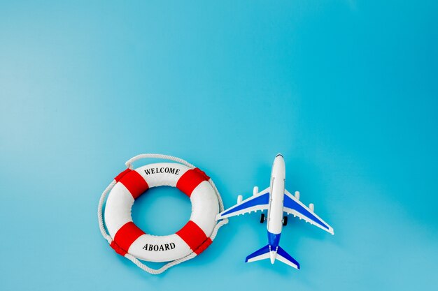 Lifebuoy and model of airplane on blue background. Summer or vacation concept. Copy space.