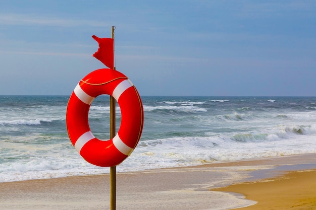 Lifebuoy and red warning flag flapping in the wind on the beach at storm a  symbol of the deterioration of the weather the danger of swimming in a stormy sea or ocean