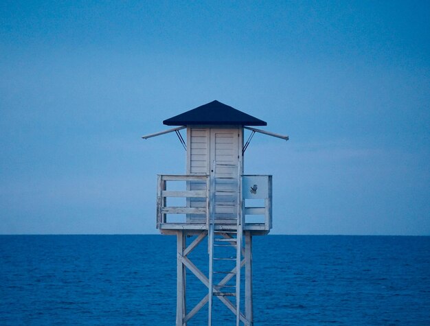 Photo lifeguard hut by sea against clear blue sky