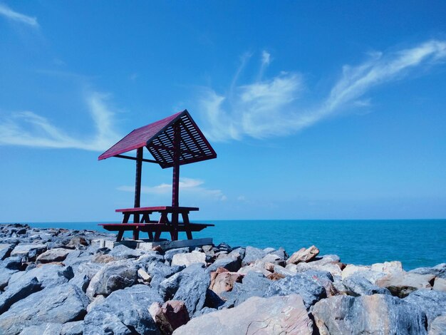 Lifeguard hut on rocks by sea against blue sky