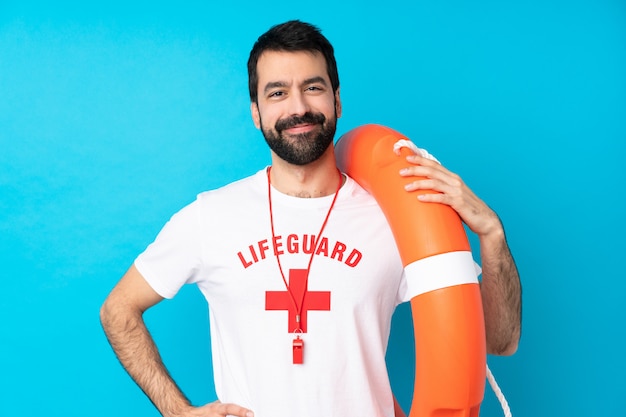 Foto uomo del bagnino sopra la posa blu con le armi all'anca e sorridere