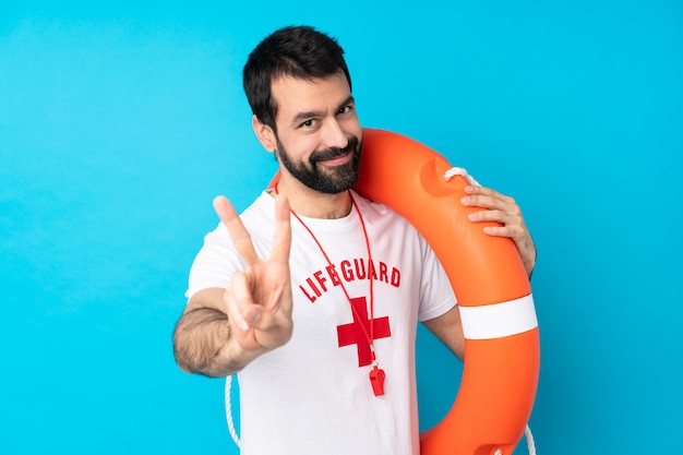 Foto uomo del bagnino sopra il blu che sorride e che mostra il segno di vittoria