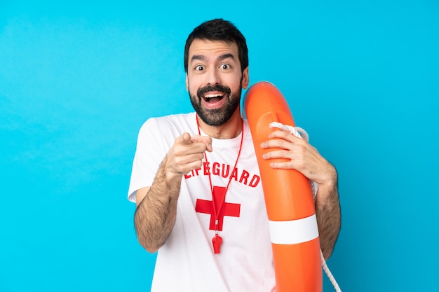 Lifeguard man over blue surprised and pointing front