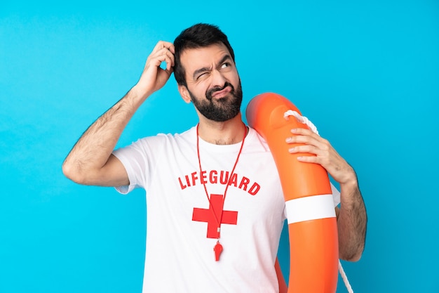 Lifeguard man over isolated blue wall having doubts while scratching head