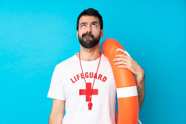 Lifeguard man over isolated blue wall and looking up