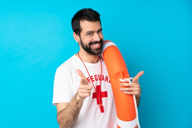 Lifeguard man over isolated blue wall pointing to the front and smiling