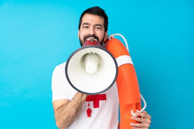 Lifeguard man over isolated blue wall shouting through a megaphone