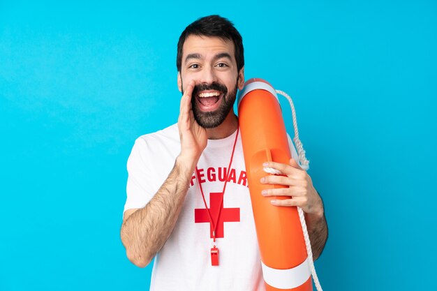 Lifeguard man over isolated blue wall shouting with mouth wide open