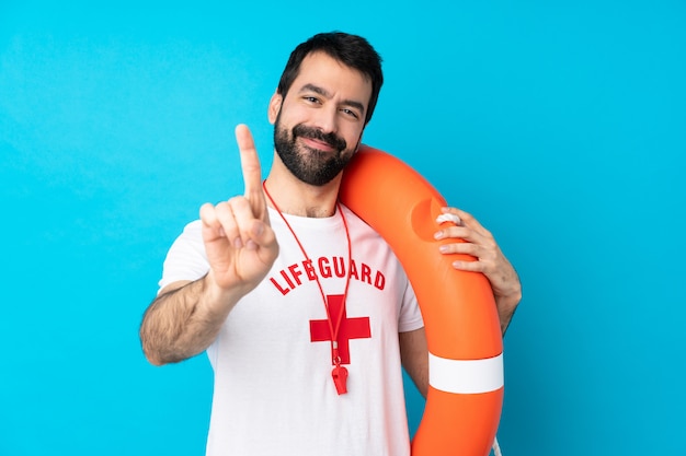 Lifeguard man over isolated blue wall showing and lifting a finger