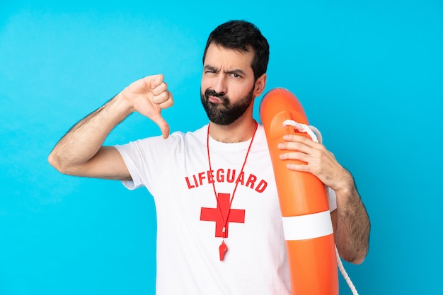 Lifeguard man over isolated blue wall showing thumb down