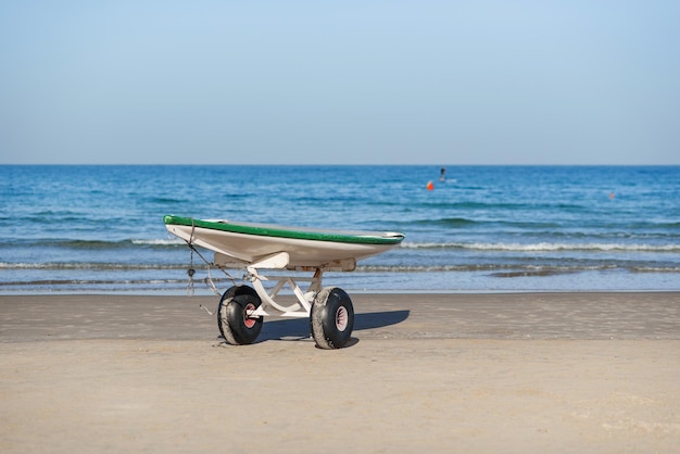 砂浜に車輪が付いたスタンドにオールが付いたライフガードサーフレスキューサーフボードが海を閉じる