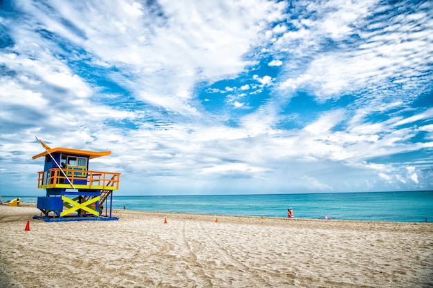 Lifeguard tower for rescue baywatch on south beach in Miami, USA. Red and blue wooden house on sea shore on cloudy sky background. Summer vacation and resort. Public guarding and safety concept