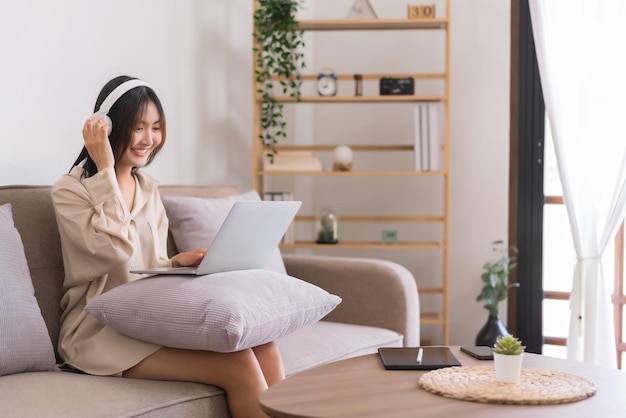 Lifestyle at home concept Jonge Aziatische vrouw draagt een koptelefoon en luistert naar muziek op laptop